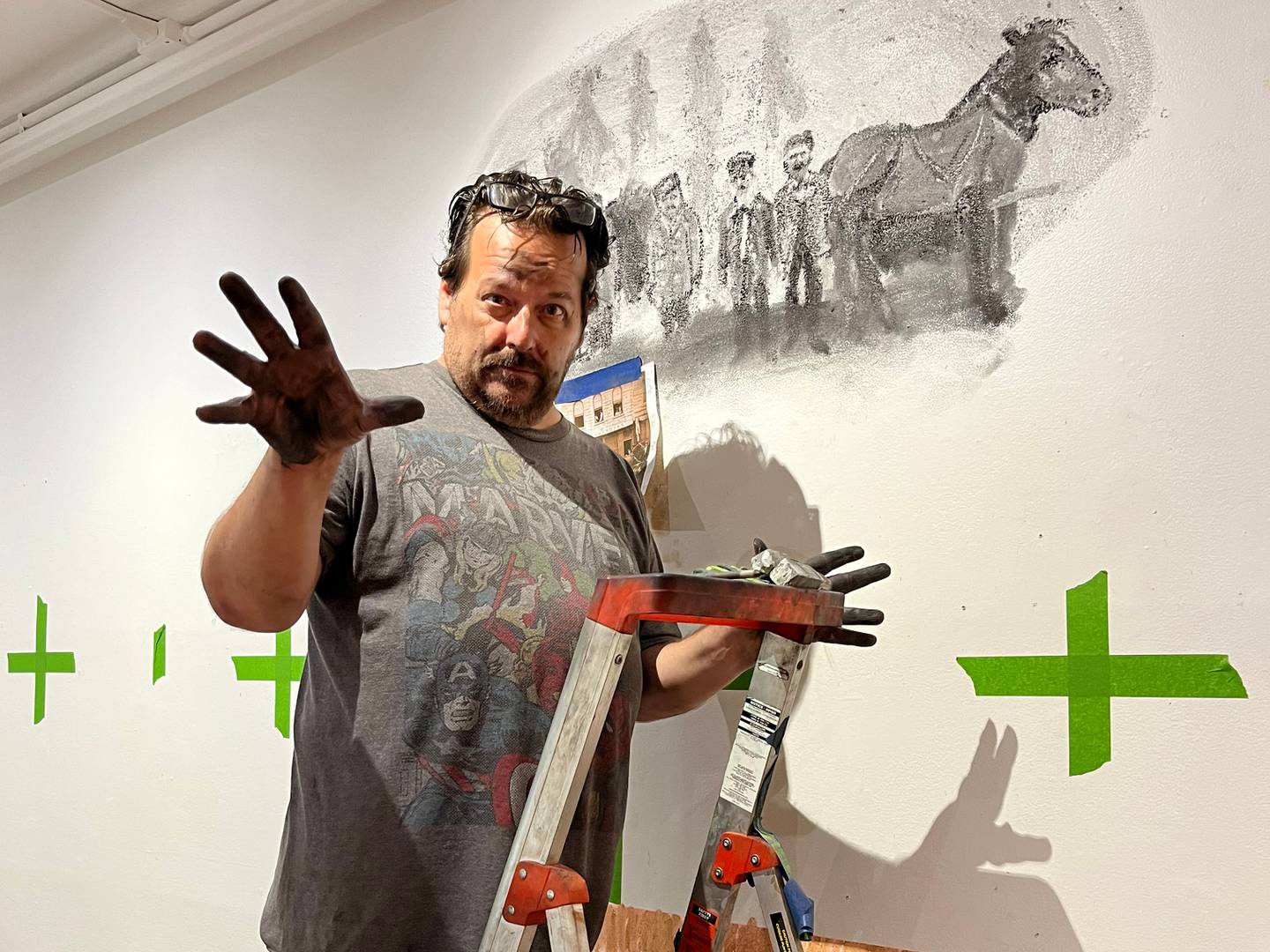 Artist Kevin Traynor shows his chalk-covered hands while working on shading a portion of the Rise from Ruins mural.
