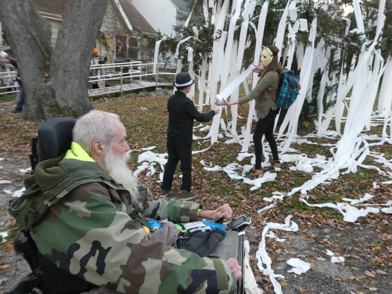 McCullom Lake resident Kerry Neff, 61, shown here with his grandson, Joe Jakubowski, and daughter, Lacey, looks on in amusement at the annual teepeeing of his tree on Monday, Oct. 31, 2022, a tradition that Neff said has lasted over 20 years.