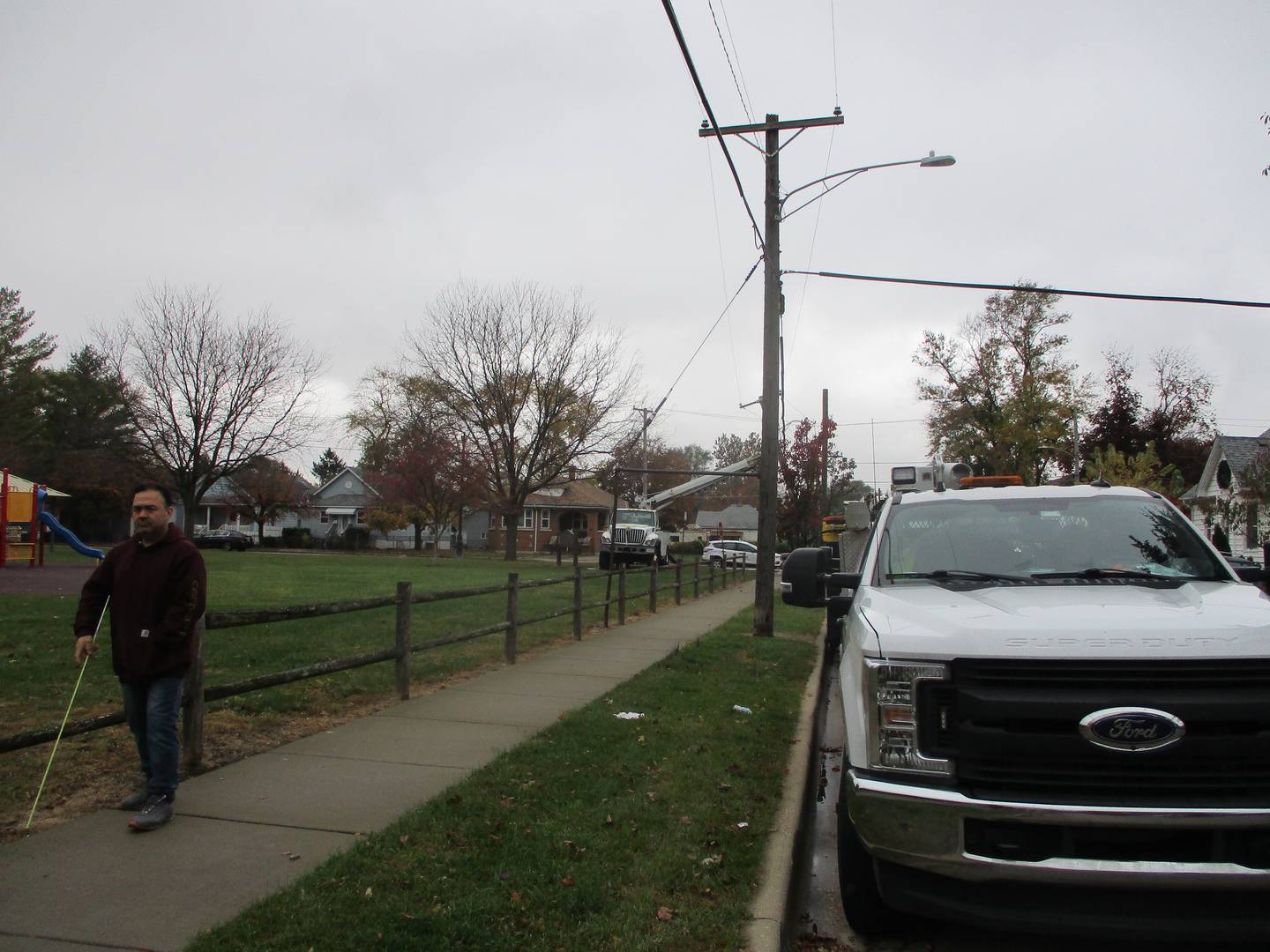 A man walks along the perimeter of Desmond Park where ComEd trucks are lined up to replace a utility pole knocked down by a man shot to death on Sunday before his car crashed into the Joliet park. Oct. 31, 2022.