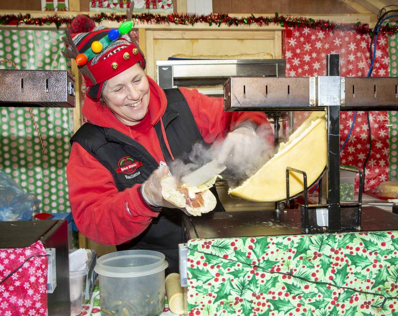 Judy Kozlowski spreads melted cheese on a baguette as she makes a raclette sandwich Sunday, Dec. 5, 2021, afternoon in the Baked Cheese Haus hut at Ottawa's Chris Kringle Market in the Jordan Block.