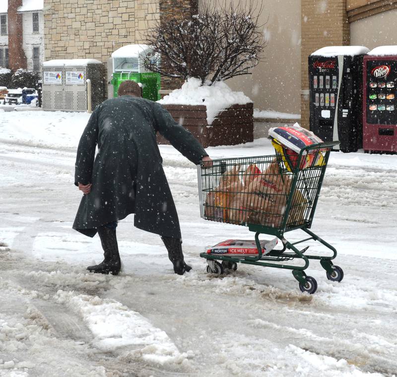 A customer pulls his cart across the snow-covered parking lot at the Oregon SuperValu grocery storm in Oregon on Friday, Jan. 12, 2024. Store owner Jim Kaufman and another employee were shoveling the entrance to the store before going over to help the man. Plow trucks had trouble keeping parking areas and roads clear as more than 6 inches of snow fell across the region on Friday with more snow forecast through the night.