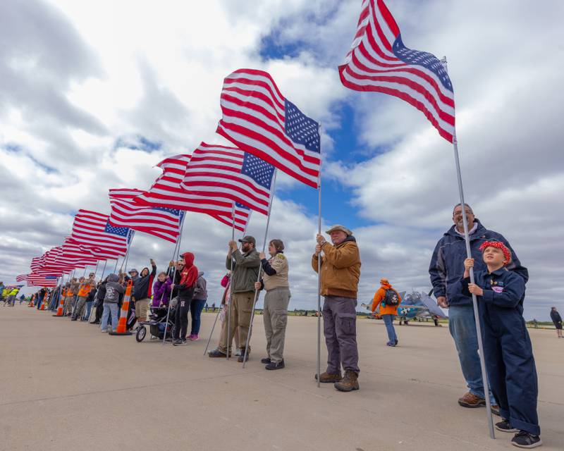 Everleigh Hickey, dressed as Rosie the Riveter steadies her flag against the heavy winds in preparation for the veterans parade at the 10th annual TBM Avenger Reunion and Airshow on Saturday, May 17, 2025 at the Illinois Valley Regional Airport in Peru.