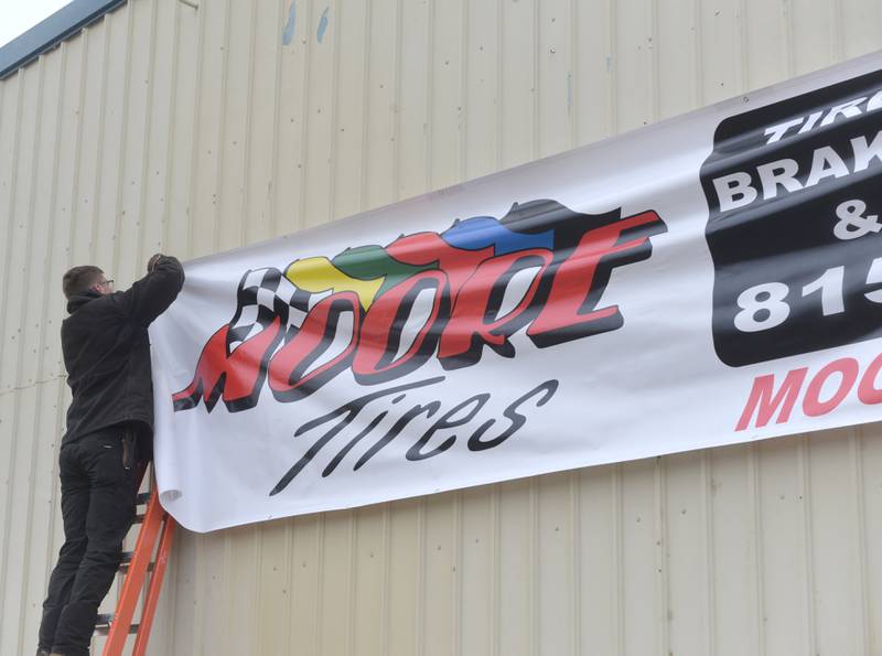 Kyle Moore secures a Moore Tires banner to the business' new location on Tuesday, Feb. 6, 2024.