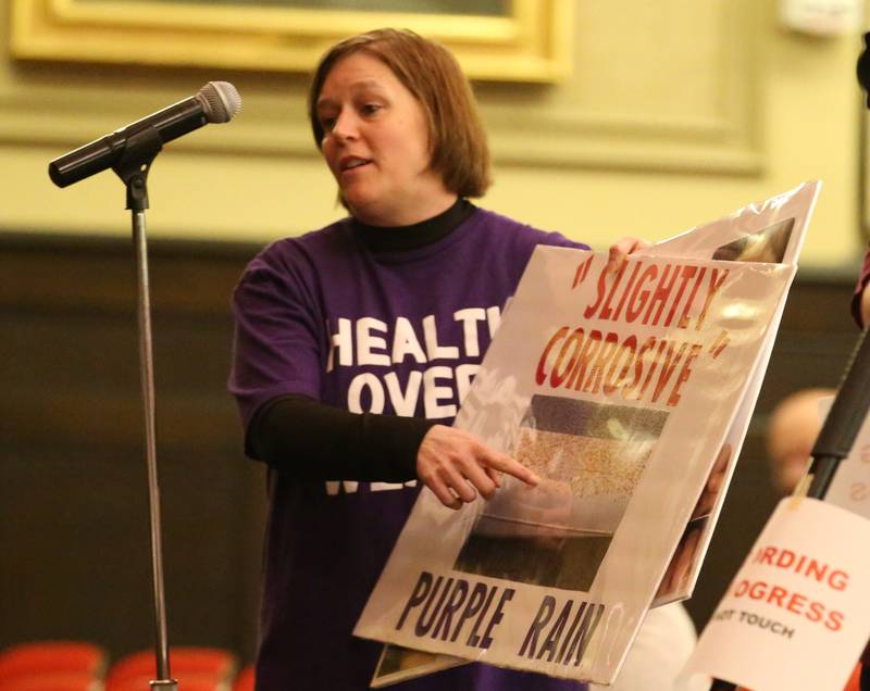 Dena Hicks, holds a sign with a photo of her pool covered in corrosive material while speaking during the Carus town hall meeting on Wednesday, May 10, 2023 in Matthiessen Auditorium at LaSalle-Peru Township High School.