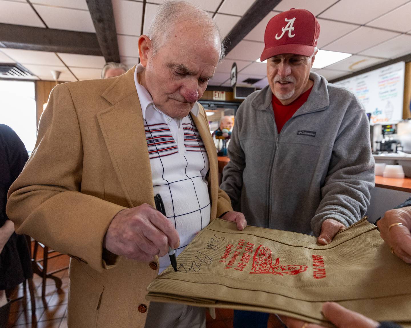 Sam Leone sings a Sam’s Pizza tote bag as Gary Hitchens watches on at Sam’s retirement celebration on Saturday, October 25, 2025 at the Rootbeer Stand in Oglesby.