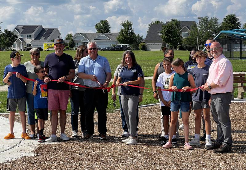 Sycamore Park District Board of Commissioners Bill Kroeger cuts the ribbon for Reston Ponds Parks on July 12, 2024. He was accompanied by children who had been playing in the park when local officials and State Rep. Jeff Keicher, R-Sycamore, gathered to celebration the park's creation.