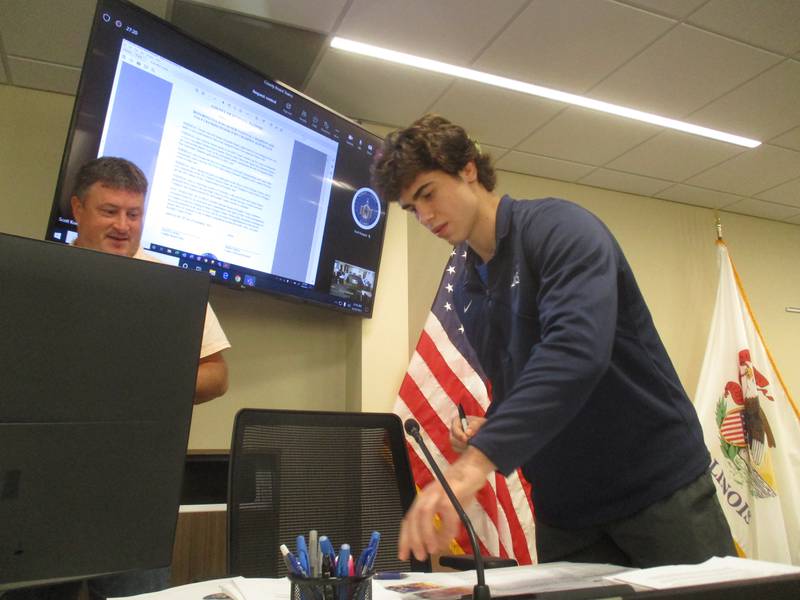 Judo champion Alex Knauf of Yorkville autographs trading cards of himself for the Kendall County Board on Sept. 20. Looking on is county board member Matt Kellogg.