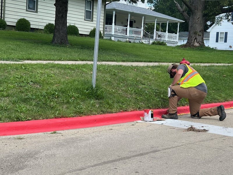 A city of Mendota worker paints a curb bright red near Northbrook School on Tuesday, Aug. 15, 2023.