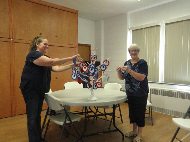 Sandra Davis (left) and  Susan Florschuetz place their patriot’s ornament on the chapter patriot tree during a recent meeting of the Fort du Rocher Chapter of the Daughters of the American Revolution.