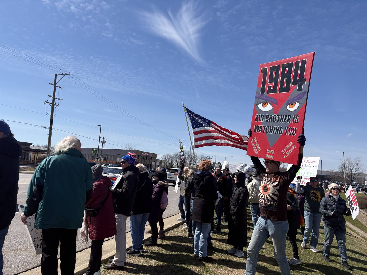 Jeff Schumacher, right, holds up a "1984" sign at a No Kings rally in Crystal Lake, Saturday, March 28, 2026.