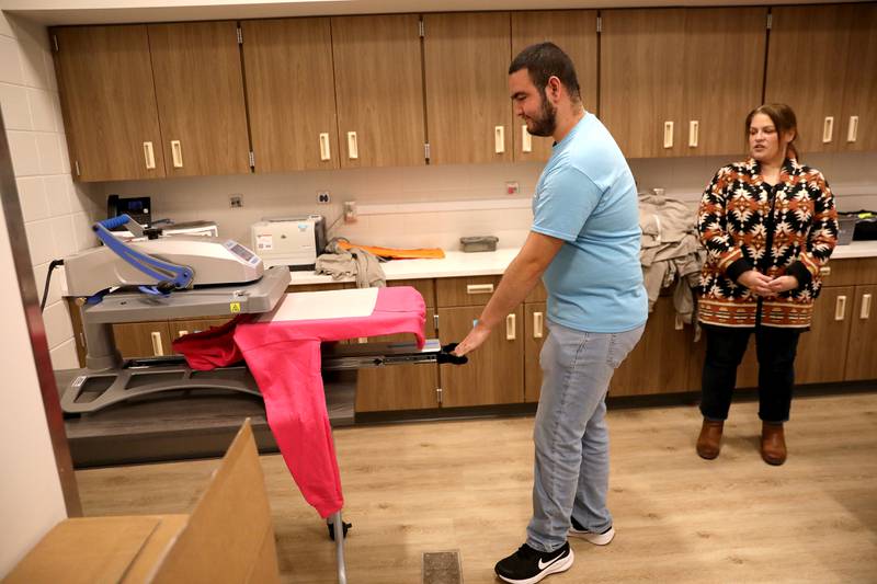 St. Charles School District 303 transitions program student Roman Rodriguez shows how he uses a press to make custom shirts as Transitions Program Chairperson Anne Federici Dragosh looks on at the former Abraham Lincoln School in St. Charles. The building underwent major renovations this summer to transition to housing the Transition Program and collaborative space for educators after a 95-year run as an elementary school.