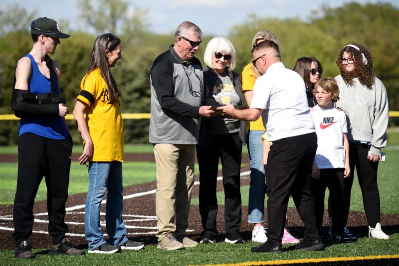 Retired Reed-Custer baseball coach Jerry Cougill, third from left, is presented with a replica of the bronze home plate the Comets are adding to their dugout from athletic director Nick Klein while surrounded by family during a ceremony honoring Cougill before a home game against Coal City Tuesday, May 6, 2025.