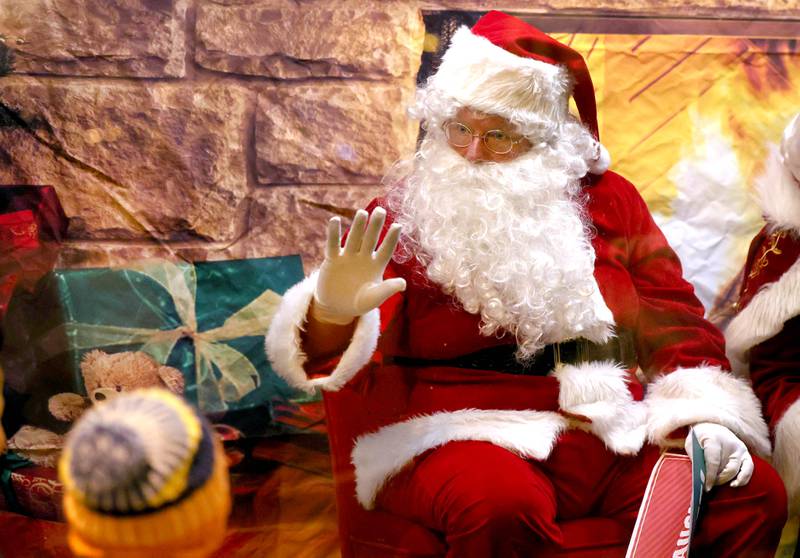 Santa Claus waves to a visitor from a window on State Street Friday, Nov. 22, 2024, during Moonlight Magic in downtown Sycamore.