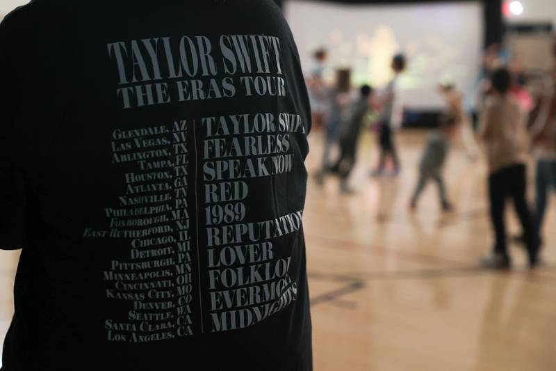 A mother wears her Taylor Swift Eras tour teeshirt as children dance at the Taylor Swift fan party hosted by the Lockport Township Park District on Saturday, Feb. 10, 2024 in Lockport.
