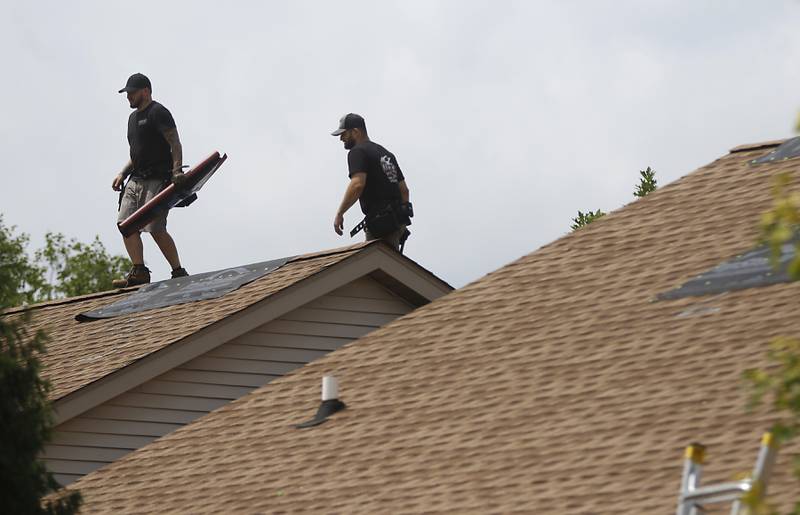 Roofers inspect the roof of a home near a damaged apartment building in Huntley on Thursday, July 13, 2023, after a confirmed tornado took the roof off the building in Huntley on Wednesday.