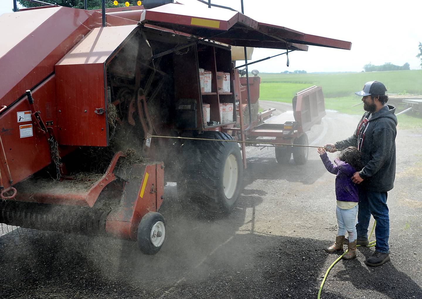 Raylee Kelly, 4, covers her eyes as he helps her dad, Bryon Kelly clean the baler Friday, June 10, 2022, on the Jacobson farm near Richmond. Kelly inherited the century-old farm from his step-grandfather Richard Jacobson.