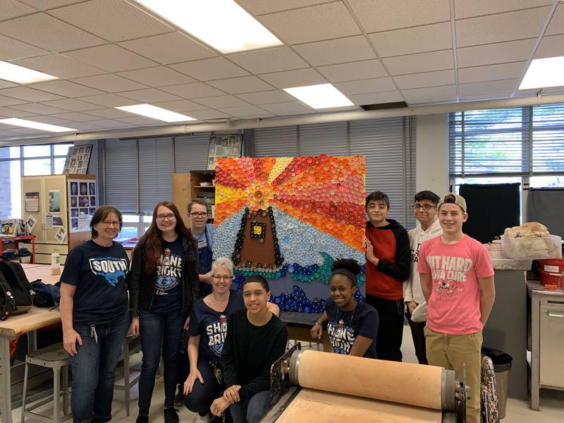 District 99 students participated in an eco-friendly art project using bottle caps, which supported the philanthropy Erica's Lighthouse. The project is an example of how the school supports the health and wellness of students and staff, which is an element of the Green Ribbon Award.
