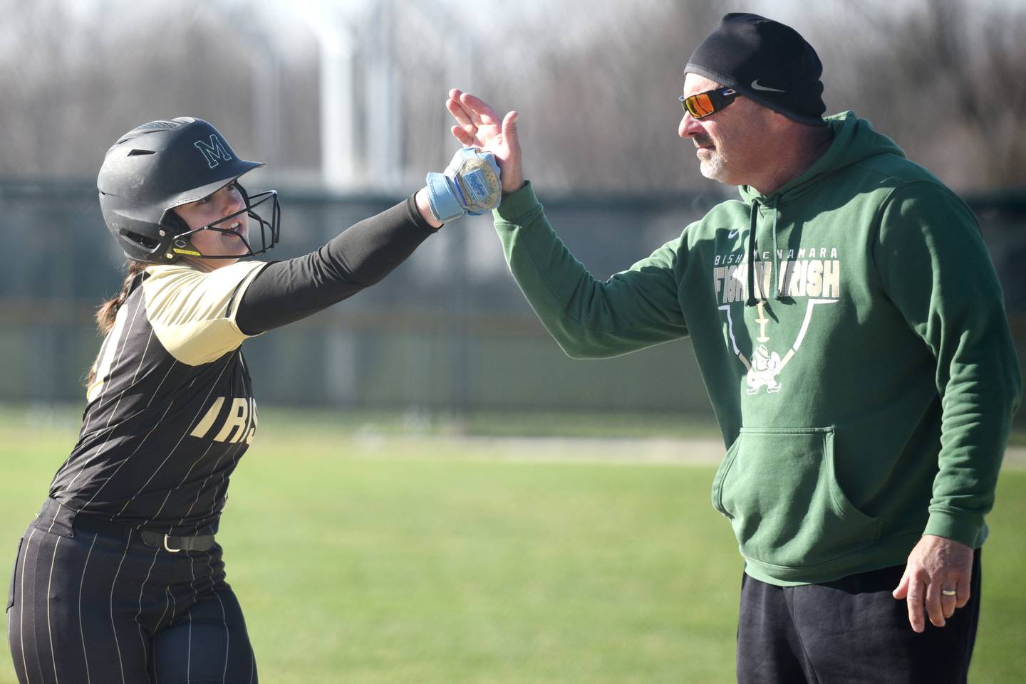 Bishop McNamara's Rhaya DePaolo, left, is congratulated by assistant coach Mike Arseneau after her first of two hits during a home game against Peotone Monday, March 23, 2026.