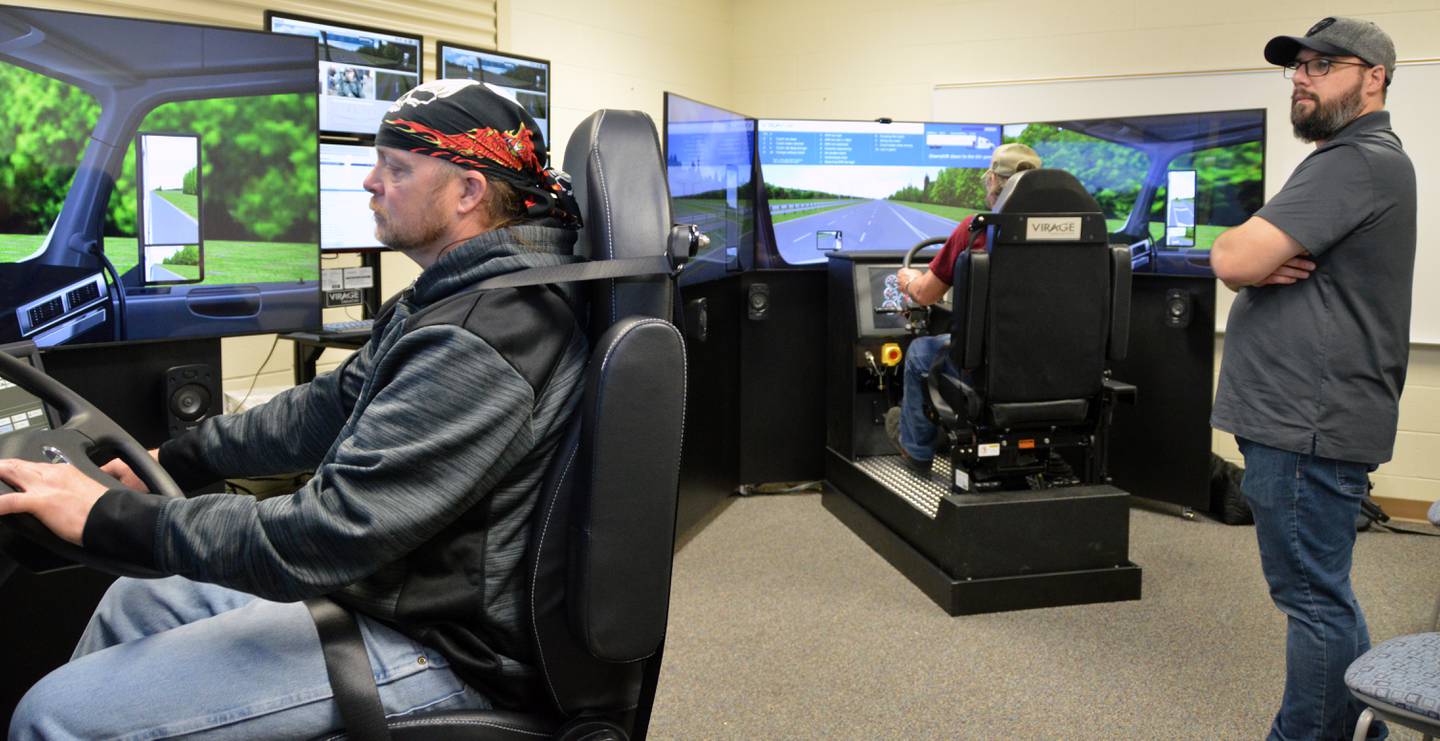 Trainers Michael Foxworthy and Richard Molln adapt to the new simulators as company representative Carl Frigault, who installed the equipment, monitors its performance. Simulators are becoming common in college and industry training programs because trainees can practice skills and experience a variety of virtual weather and driving conditions.