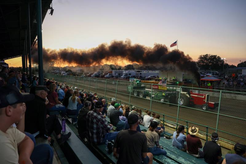 Fairgoers watch as a tractor competes in the Illinois Tractor Pulling Association Truck and Tractor Pull during the Will County Fair on Thursday, Aug. 21, 2025.