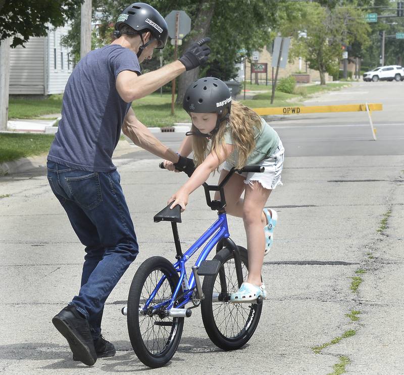 Matt Wilhelm teaches volunteer Brynn Russell a riding trick on Washington Street in Ottawa before a large crowd Thursday, July 28, 2022, during a show at the Reddick Library.