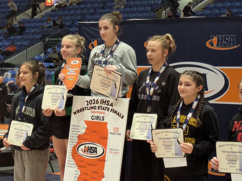 Angelina Gochis (center) stands on the podium after winning the 120-pound state championship at the IHSA Girls Wrestling State Championships on Saturday, February 28, 2026, in Bloomington.