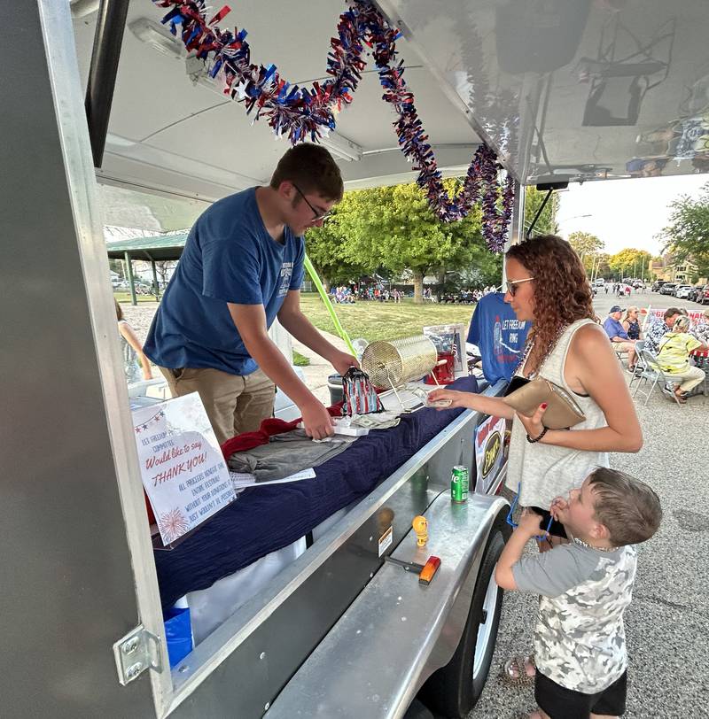 Morgan Peterson and Wesley, 4, of Mt. Morris, purchase glow sticks a soft drink from Immanuel Arrellano at the Let Freedom Ring merchandise truck during the Let Freedom Ring block party on  Friday, July 4, 2025 in Mt. Morris.