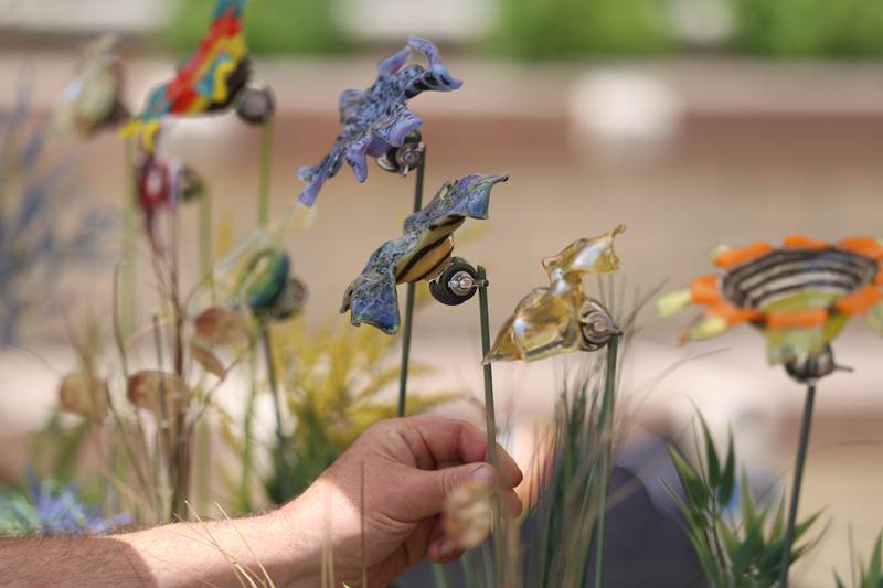 A shopper checks out a glass flower at the Regis Glass Art tent at the new city square for the farmers market on Friday, May 22, 2026 in Joliet.