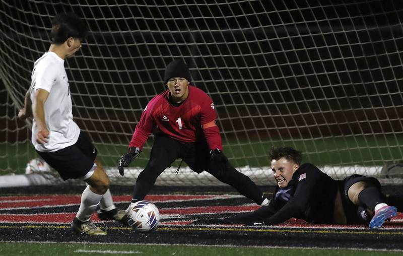 McHenry's Dylan Fischler kicks the ball away from St. Charles North's Oliver Longoszan as he hits the turf in front of McHenry goalkeeper Mason Bertone during an IHSA Class 3A Huntley Regional boys soccer semifinal match on Tuesday, Oct. 21, 2025, at Huntley High School.