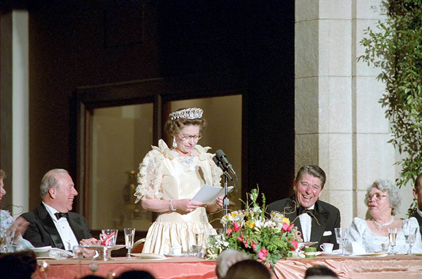 President Reagan laughs at remarks by Queen Elizabeth II at a dinner honoring her at M.H. de Young Memorial Museum in San Francisco California with George Shultz and Helena Shultz on March 1, 1983.