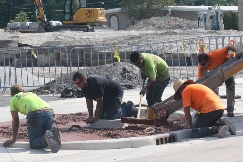 Crews work in the heat while pouring a sidewalk near the retail plaza site on Tuesday, Aug. 27, 2024 in Utica.