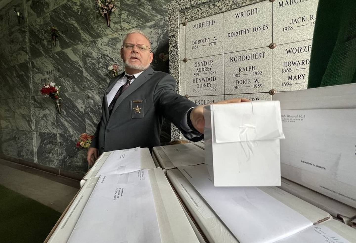 Kane County Coroner Rob Russell grabs a box of remains of a person whose unclaimed ashes will be put into an empty vault at North Cemetery in St. Charles as part of the Kane County Coroner's Community Memorial Service on May 27, 2022.