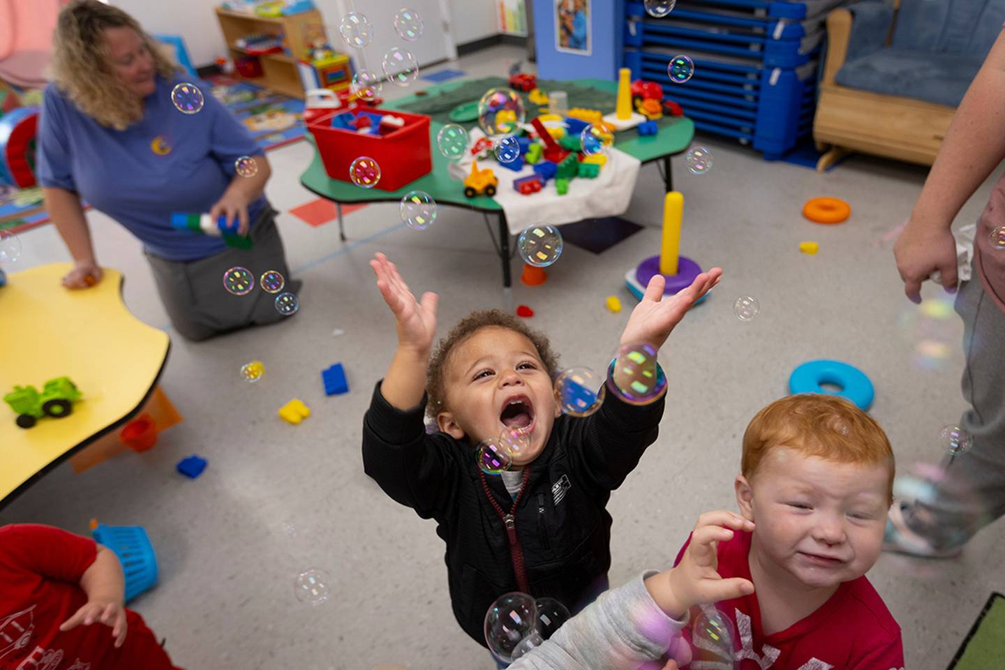 Bryce Clemons and Harper Watkins play with bubbles as Heather Casner cleans toys.