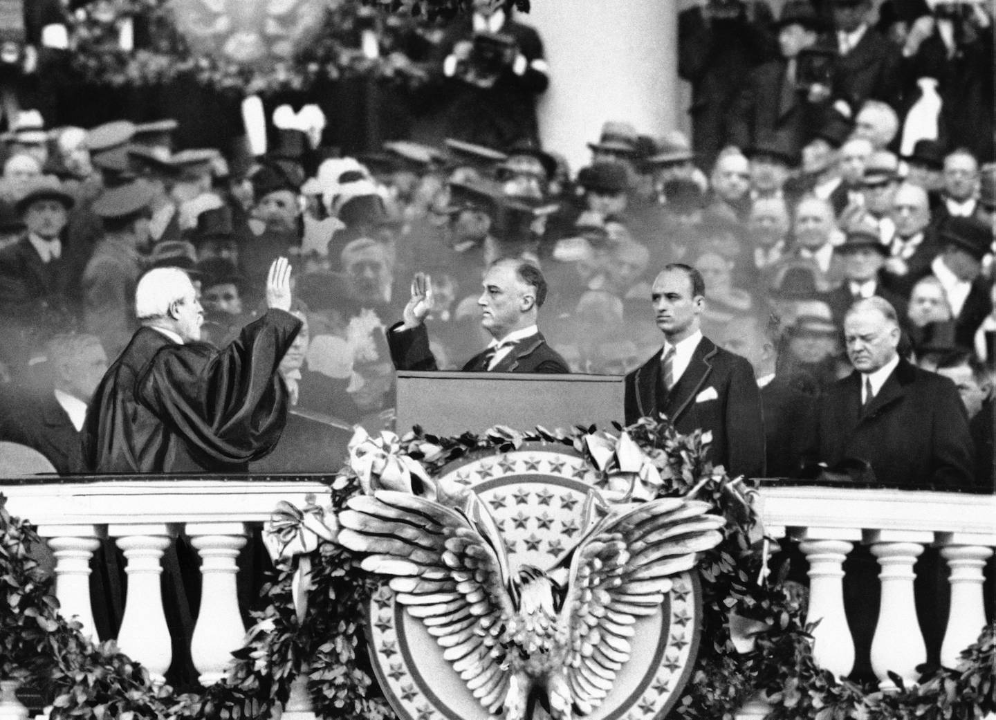 President Franklin D. Roosevelt takes the oath of office from Chief Justice Charles E. Hughes at the inauguration, March 4, 1933. At right is Herbert Hoover and behind the president is his eldest son James Roosevelt.