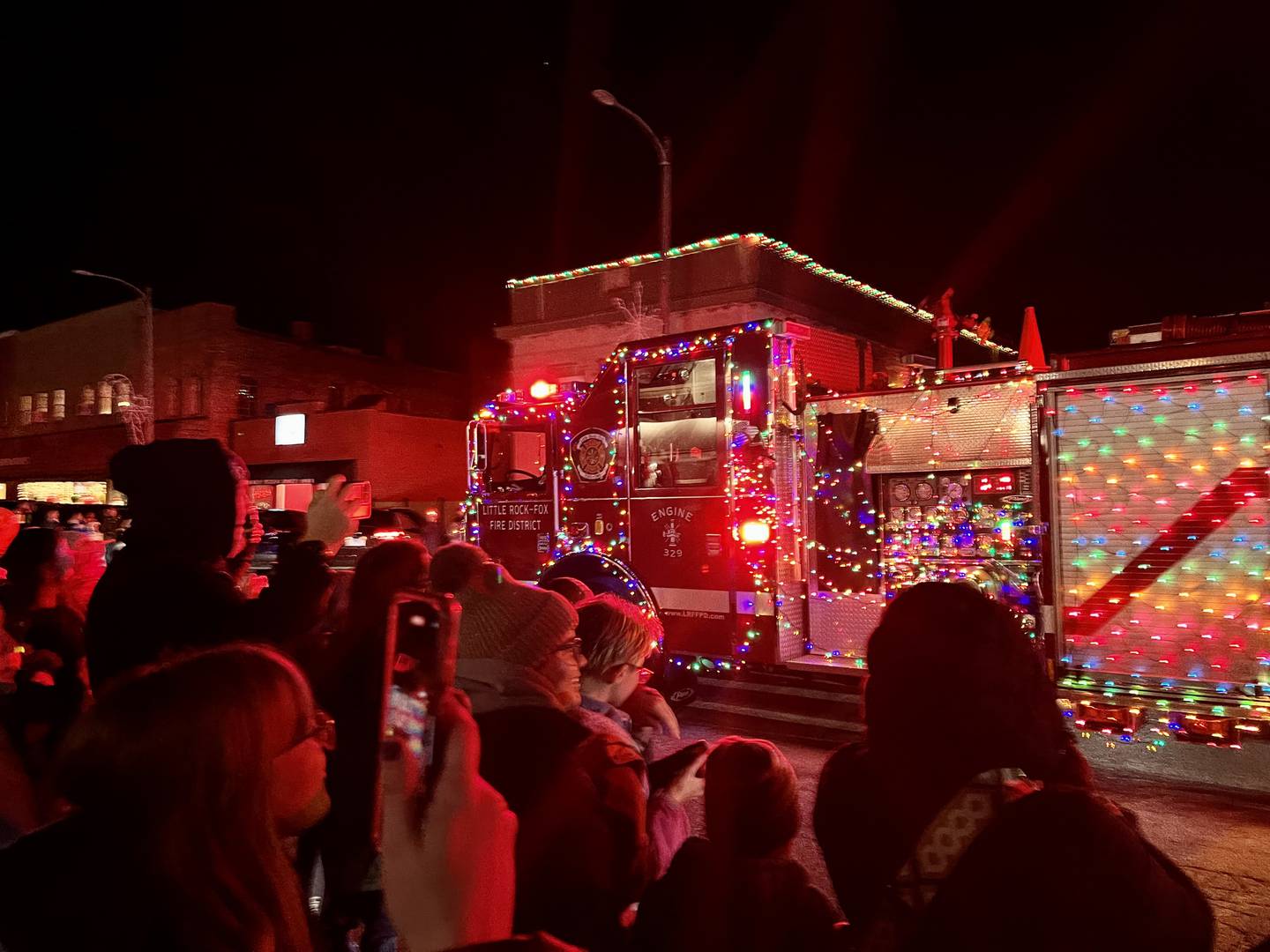Families gather during the lighted vehicle parade of Plano's Rockin' Christmas to watch a Little Rock-Fox Fire Protection District firetruck decorated with holiday lights cruise d