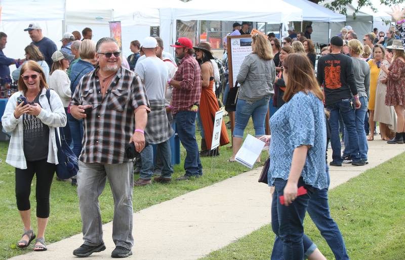 People stroll down a sidewalk while enjoying a glass of wine at the 20th annual Vintage Illinois Wine Festival on Sunday, Sept. 17, 2023 in Utica.