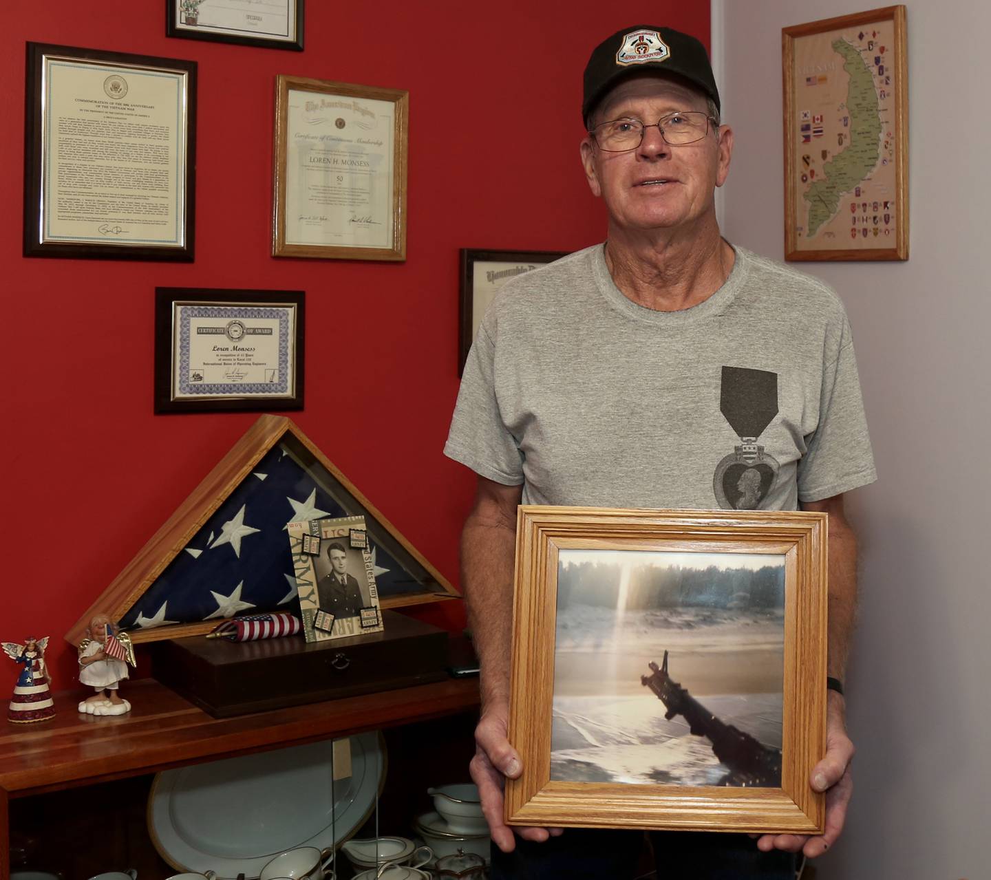 Loren Monsess poses with one of his prized possessions from his time in Vietnam, a photograph he took from his helicopter in 1970 of the coast of Vietnam.