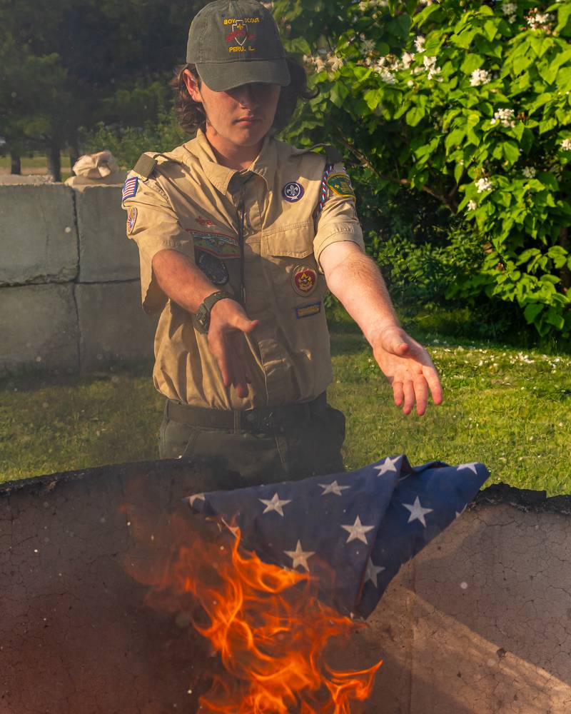 Desmond O'Dell of Scout Troop 123 releases a folded flag into the fire to be retired in the prescribed respectful matter at Veterans Memorial Park on June 14, 2025 in Peru.