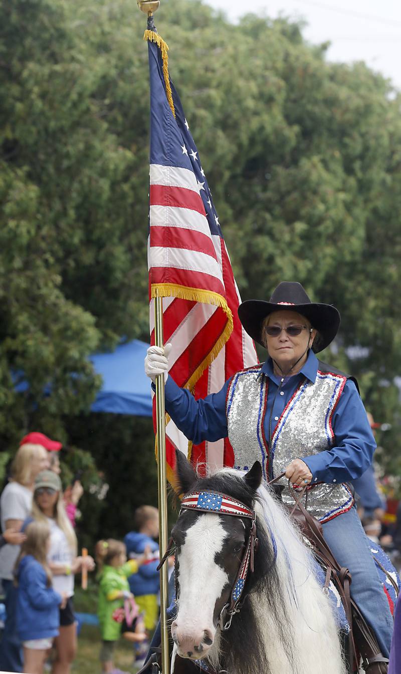 Dian McPherson carries the America Flag as he she rides her horse Sunday, July 2, 2023 during Crystal Lake’s annual Independence Day Parade on Dole Avenue in Crystal Lake. This year’s parade feature close to 100 units.