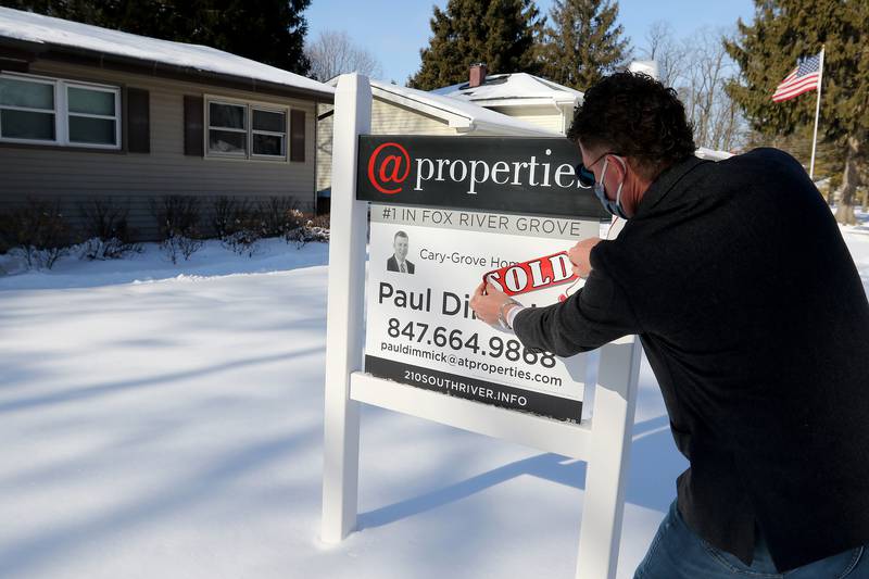 Real estate agent Paul Dimmick with @Properties attaches a sold sticker to a for sale sign on one of his recently-sold listings on Friday, Jan. 29, 2021in Fox River Grove.