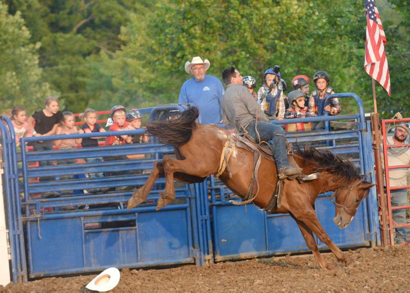 A cowboy competes in the bronc riding event as kids watch while waiting to compete in "Mutton Busting" at the T & A Bucking Bulls Rodeo at the Ogle County Fair on Friday, Aug. 1, 2025 in Oregon.