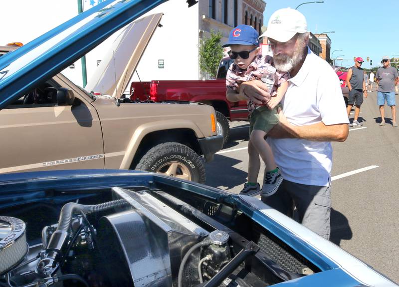 Cain Oprins, 2, from Sycamore gets a lift from his grandpa Co Oprins, also from Sycamore, to see under the hood of one of the cars on display on State Street in Sycamore Sunday, July 31, 2022, during the 22nd Annual Fizz Ehrler Memorial Car Show. Most of downtown Sycamore was filled with classic cars for the show.