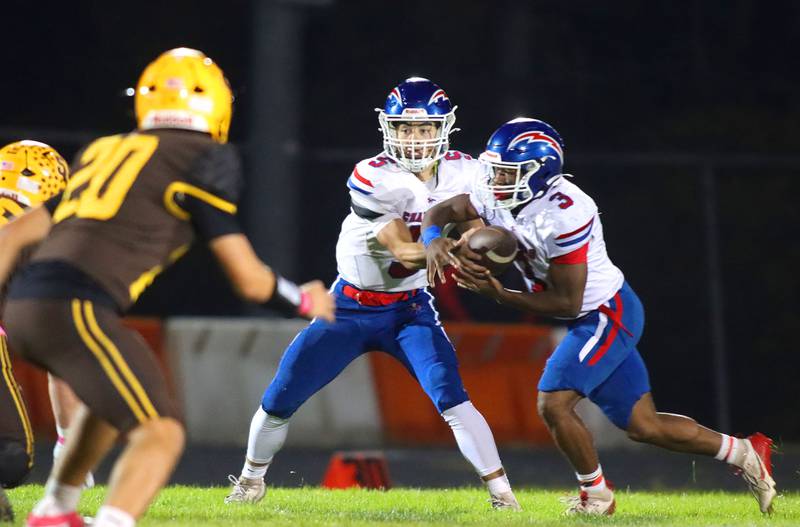 Dundee-Crown’s Isaac Grzynkowicz, center, hands the ball off to Kadin Malone in varsity football  at Jacobs High School in Algonquin on Friday, Oct. 10, 2025.