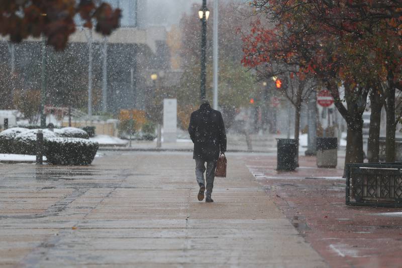 Snow falls as a business man walks along West Jefferson Street in downtown Joliet on Thursday, Nov. 21, 2024.