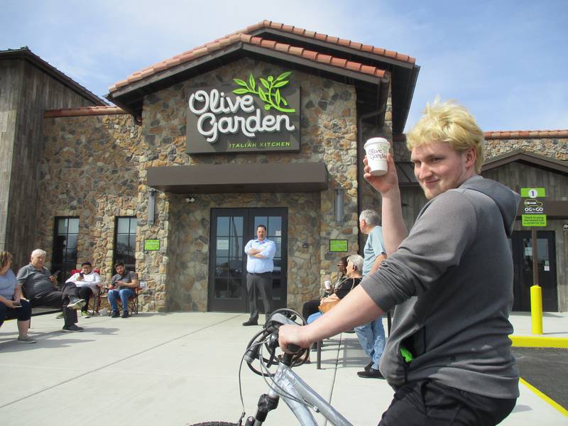 Nathan Ditton of Joliet raises an Olive Garden cup outside the Joliet restaurant on the bicycle that he used to peddle for 30-mile round trips to the Bolingbrook Olive Garden before the restaurant chain opened closer to home on Monday, April 10, 2023.