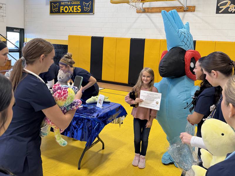 A Nettle Creek Elementary student celebrates her stuffed animal getting a clean bill of health by getting a picture with Benny the Blue Bird.
