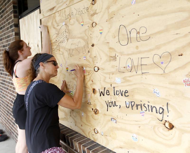 Jacqui Murk, right, of Crystal Lake, and her daughter, Izzie, write notes of support on the boarded up window at Uprising Bakery & Cafe in Lake in the Hills, on Monday, July 26, 2022, after the store reopened Sunday after its front windows were smashed and epithets written on the walls, to long lines and enthusiastic community support. The cafe, which was planning to host an all-ages drag show Saturday night, had experienced backlash over the previous few weeks.
