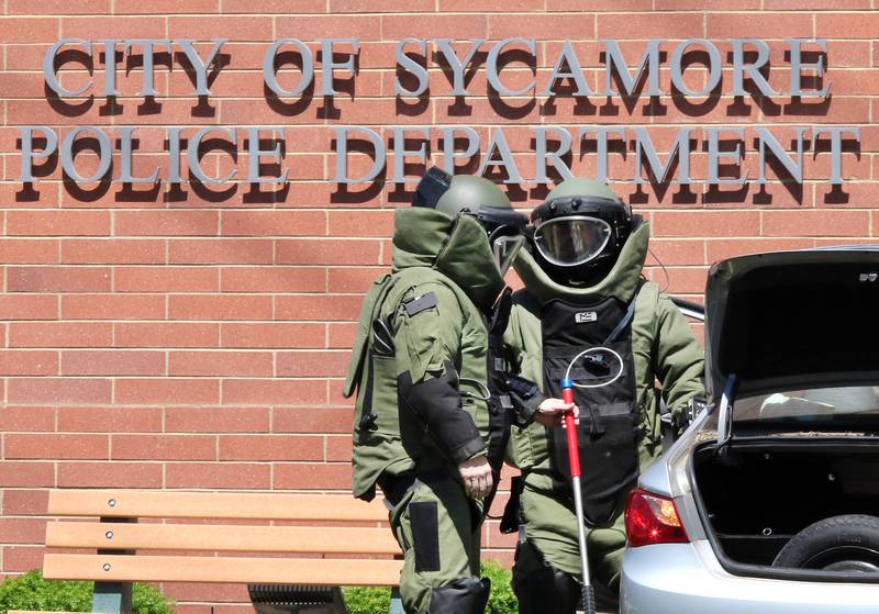 Officers in protective gear search a car Wednesday May 26, 2021, that crashed into the Sycamore Police Department on DeKalb Avenue. Law enforcement from several agencies are on hand investigating, and the cause of the crash remains unknown at this time.