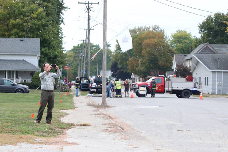 A resident takes a photo as a crew sets up road closure signs following a concrete grain bin collapse on Wednesday, Oct. 15, 2025, at the Donovan Farmers Co-Op Elevator in downtown Martinton.