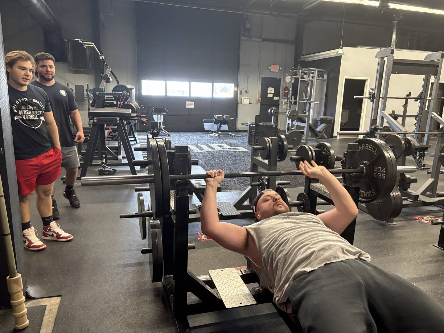 Anthony, left, and DJ Yatos watch as Nick Bos lifts weights at Warhouse Barbell in Huntley Sept. 3, 2025.